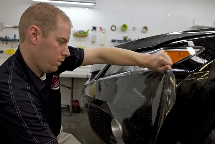 Technician applying paint protection film to a vehicle's front bumper