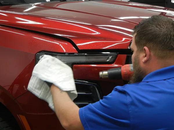 Technician using a heat gun to conform paint protection film near a headlight