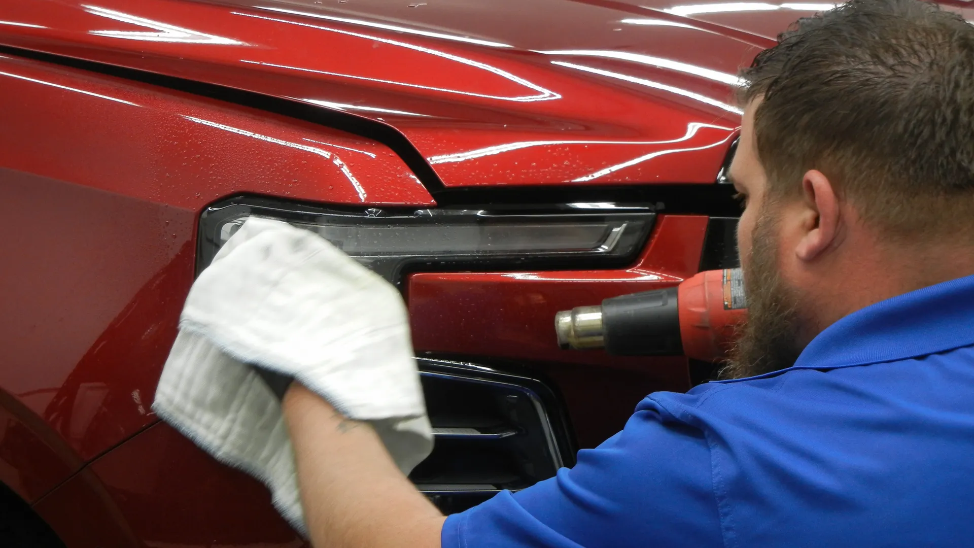 Technician using a heat gun to conform paint protection film near a headlight