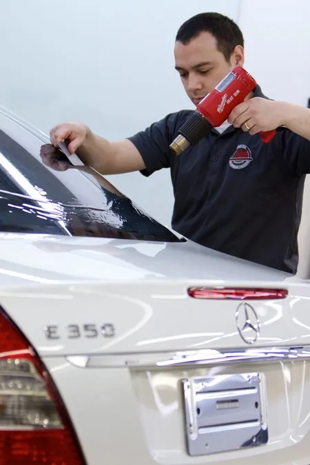 Technician applying window tint film to a vehicle's rear windshield