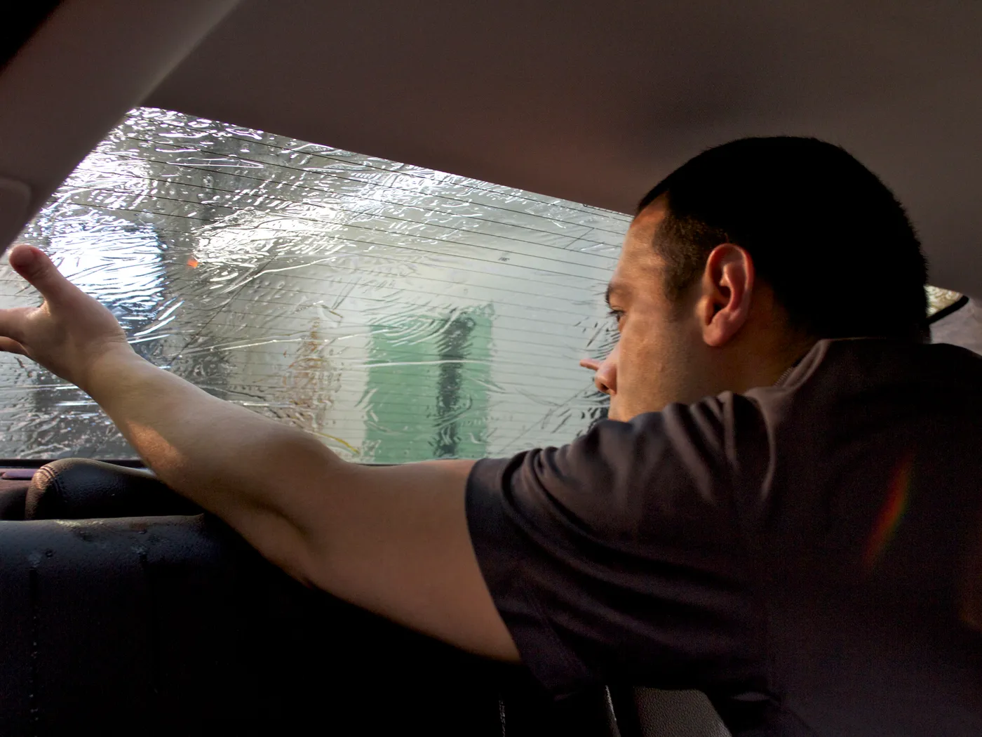 Technician applying tint film from inside a vehicle's rear window