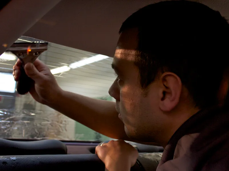 Technician using a squeegee to smooth tint film inside a vehicle