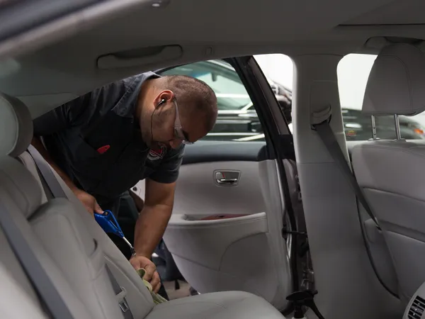 Technician detailing a sedan's rear seatbelt and door area